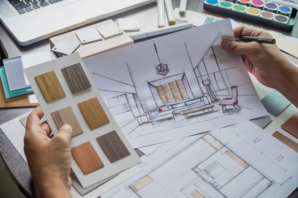 Architecte d'intérieur travaillant sur esquisse perspective d'un salon moderne, tenant stylo noir, consultant échantillons matériaux bois