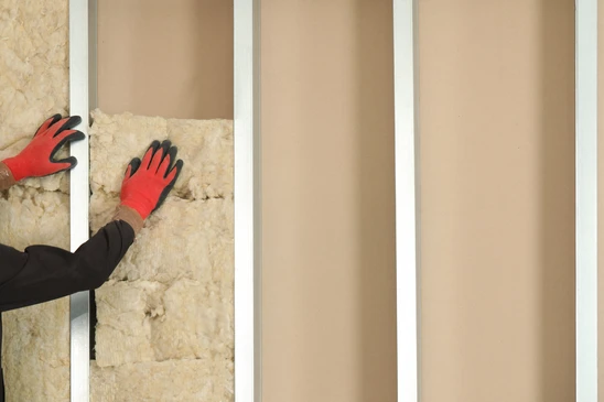 Ouvrier en combinaison bleue installant de l'isolant thermique jaune dans les combles d'une habitation