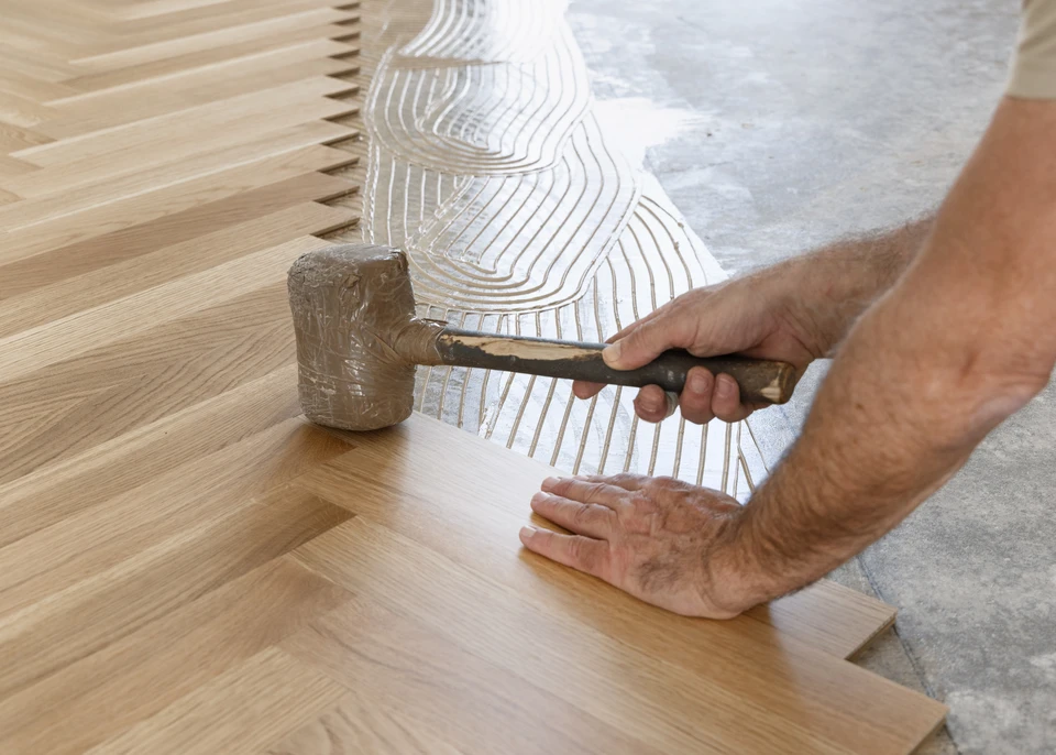 Un artisan en combinaison de travail posant des plaques de plâtre sur une cloison intérieure dans un petit espace étroit (couloir ou alcôve), montrant la précision et la rigueur du travail en espace réduit. L'artisan est à genoux ou accroupi, appliquant ou ajustant les plaques. La scène capture l'attention aux détails et l'expertise artisanale adaptée aux petites surfaces, dans le contexte de la plâtrerie et rénovation intérieure.