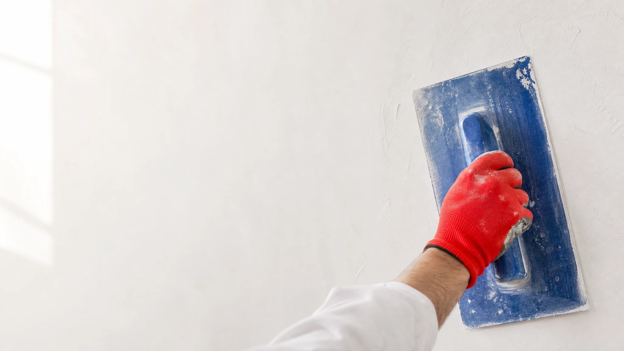 Ouvrier en tenue de travail installant des panneaux de placo sur mur intérieur, chantier de construction avec mur en briques apparentes